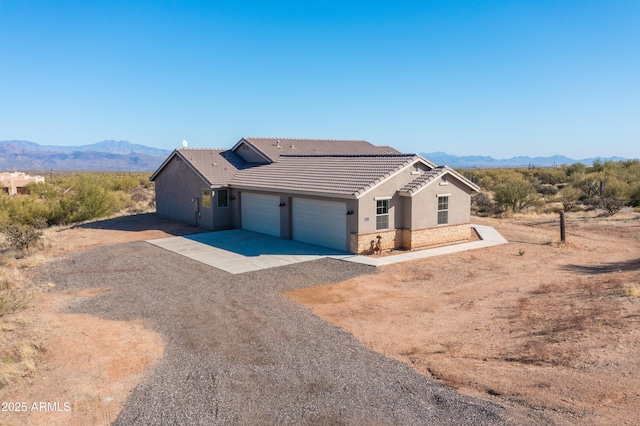 ranch-style house featuring a tile roof, stucco siding, concrete driveway, a mountain view, and stone siding