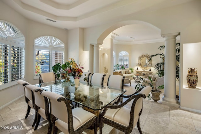 dining room featuring a raised ceiling, ornate columns, crown molding, and a wealth of natural light