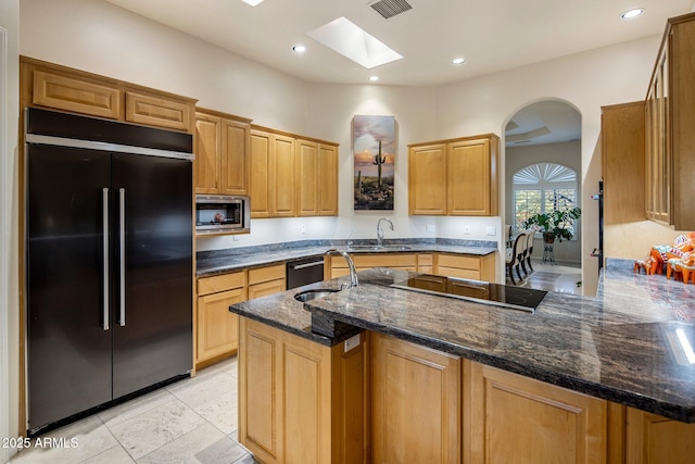 kitchen featuring dark stone counters, a skylight, sink, and black appliances