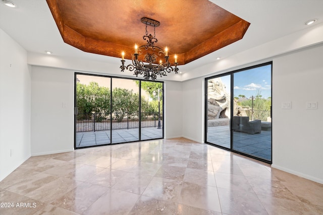 empty room with a raised ceiling, plenty of natural light, and a chandelier