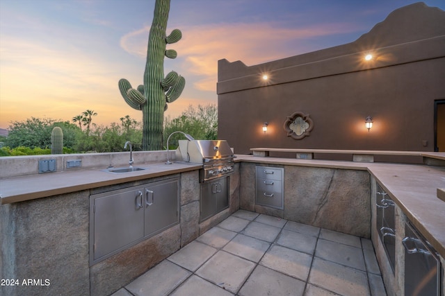 patio terrace at dusk with area for grilling, sink, and exterior kitchen