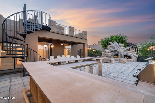 pool at dusk with a bar, an outdoor kitchen, area for grilling, and a patio