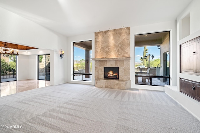 unfurnished living room with a wealth of natural light, a large fireplace, light colored carpet, and a notable chandelier