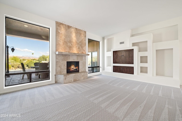 unfurnished living room featuring a tile fireplace, carpet, plenty of natural light, and built in features