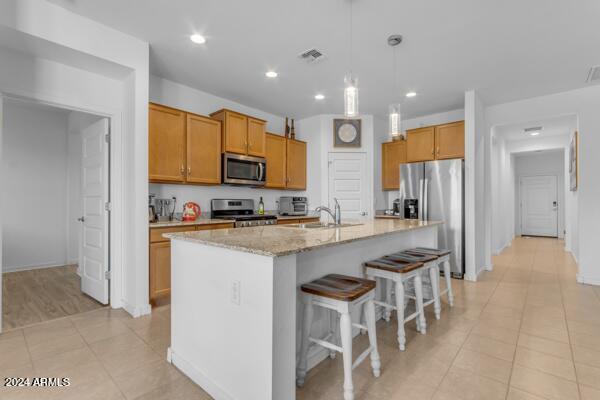 kitchen with light tile patterned floors, a kitchen island with sink, stainless steel appliances, sink, and light stone counters