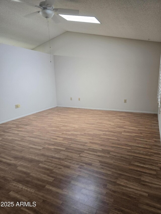 unfurnished room with dark wood-type flooring, baseboards, ceiling fan, and vaulted ceiling with skylight