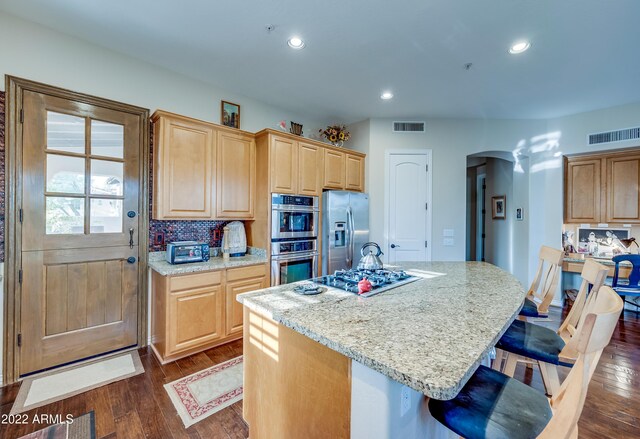 kitchen featuring appliances with stainless steel finishes, a kitchen island with sink, dark hardwood / wood-style flooring, and a breakfast bar