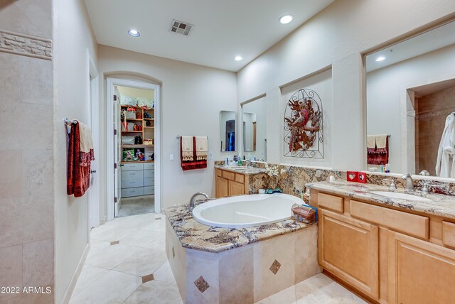 bathroom featuring tile patterned flooring, tiled bath, and vanity