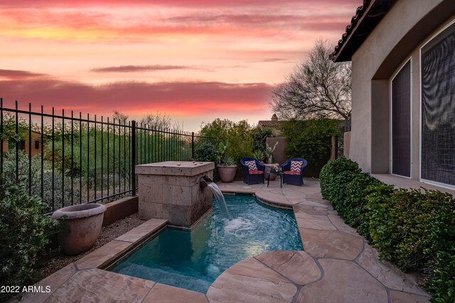 pool at dusk featuring pool water feature and a patio area