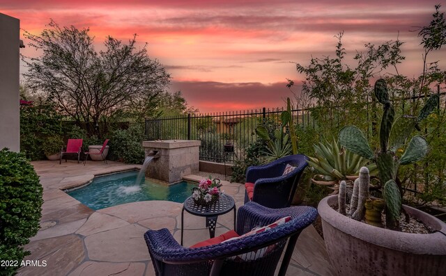 pool at dusk featuring pool water feature and a patio