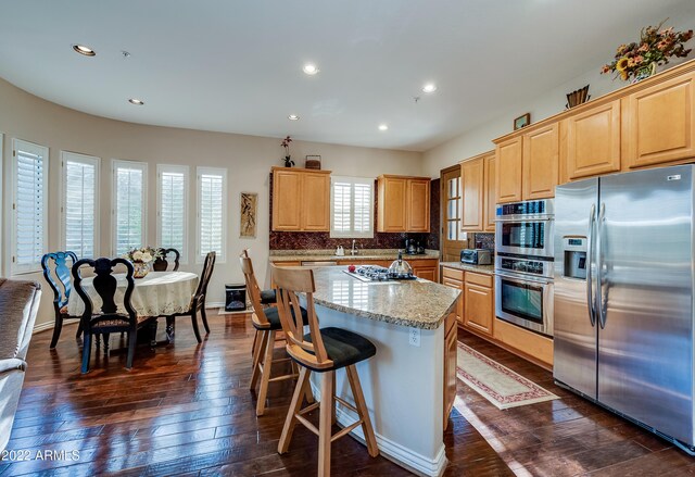 kitchen featuring appliances with stainless steel finishes, a healthy amount of sunlight, a center island, and dark hardwood / wood-style flooring