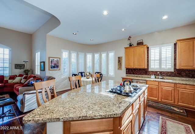 kitchen with dark wood-type flooring, sink, tasteful backsplash, stainless steel gas cooktop, and a kitchen island