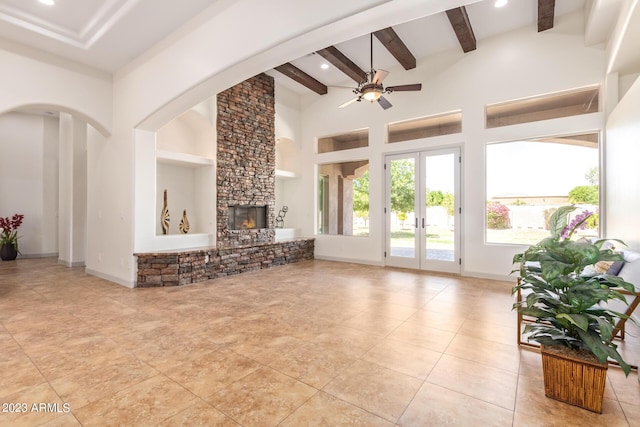 tiled living room with beam ceiling, ceiling fan, french doors, a stone fireplace, and a towering ceiling