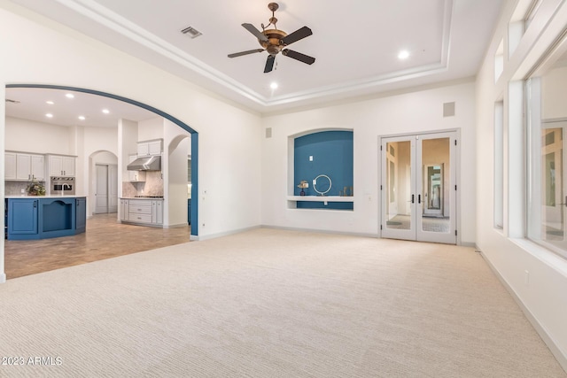 unfurnished living room with ceiling fan, light carpet, a high ceiling, and a tray ceiling