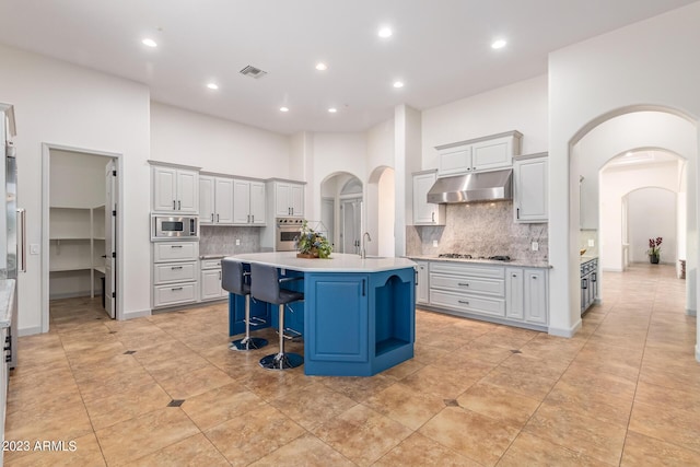 kitchen featuring backsplash, a high ceiling, an island with sink, appliances with stainless steel finishes, and a breakfast bar area