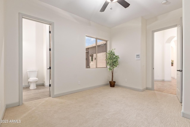 bedroom with ceiling fan, light colored carpet, and ensuite bath