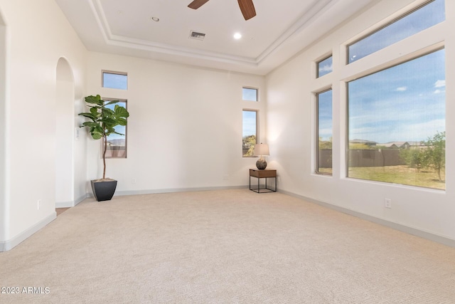 carpeted empty room with ceiling fan, a towering ceiling, and a tray ceiling