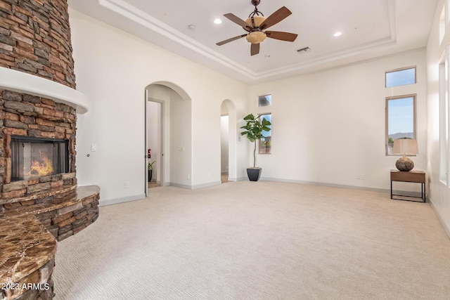 living room with light carpet, a raised ceiling, ceiling fan, and a stone fireplace