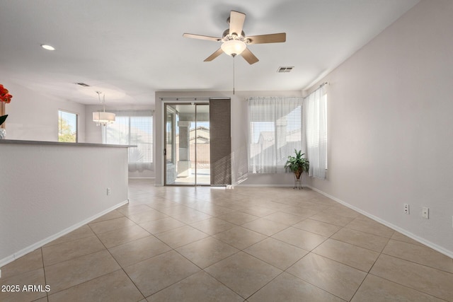 tiled empty room with ceiling fan with notable chandelier and a wealth of natural light