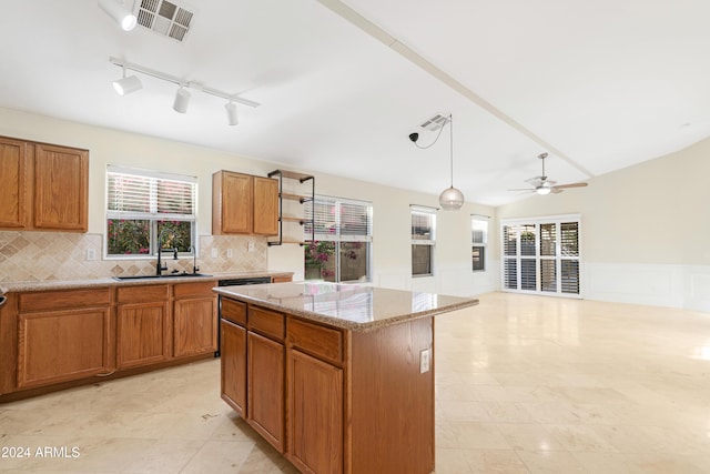 kitchen with sink, a kitchen island, pendant lighting, light stone counters, and lofted ceiling