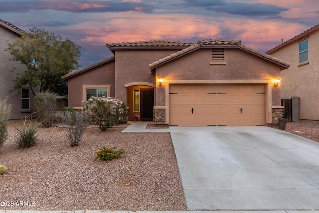 mediterranean / spanish house featuring concrete driveway, stone siding, a tiled roof, an attached garage, and stucco siding