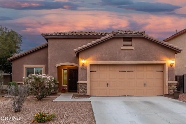 mediterranean / spanish house featuring a garage, stone siding, a tiled roof, concrete driveway, and stucco siding