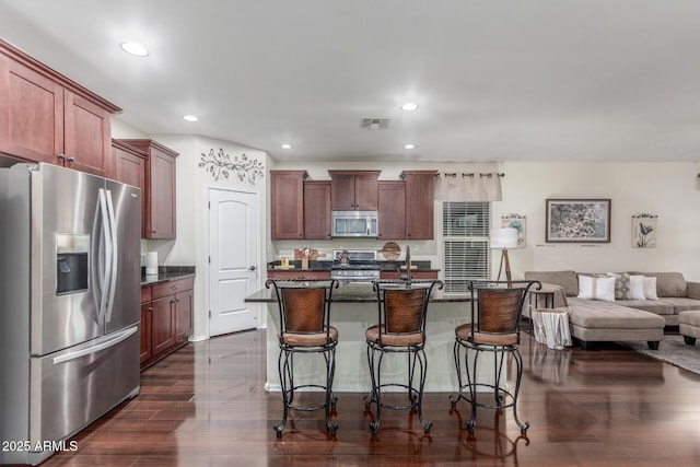 kitchen featuring recessed lighting, a breakfast bar, stainless steel appliances, dark countertops, and open floor plan