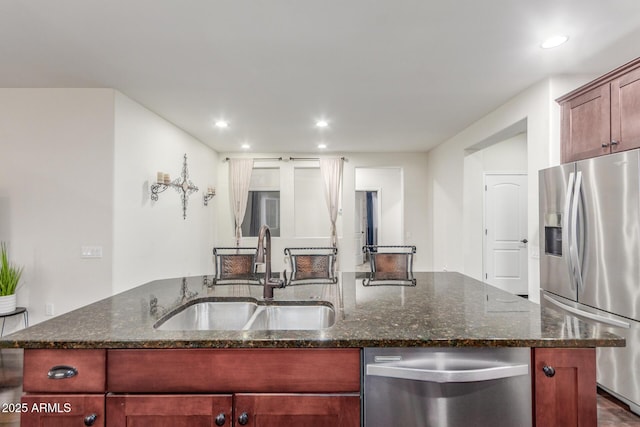 kitchen featuring dark stone counters, a sink, appliances with stainless steel finishes, recessed lighting, and a kitchen island with sink