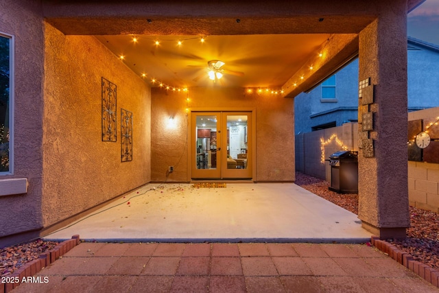 view of exterior entry featuring stucco siding, fence, a patio, and french doors