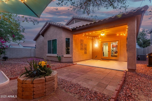 back of property at dusk featuring fence, cooling unit, a patio, a tile roof, and stucco siding