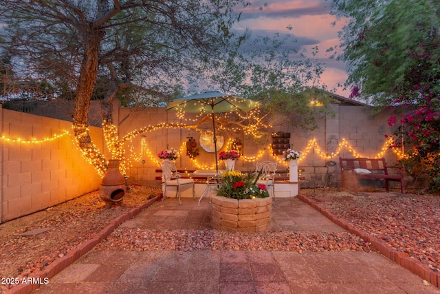 yard at dusk with a fireplace, fence, and a patio area