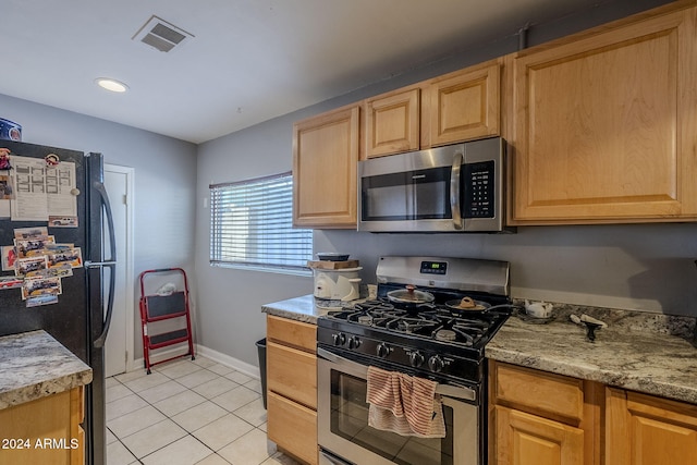 kitchen with light stone countertops, appliances with stainless steel finishes, light brown cabinetry, and light tile patterned flooring