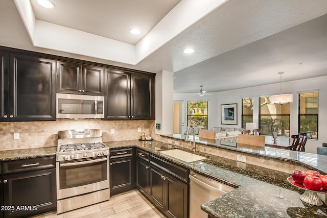 kitchen featuring stainless steel appliances, a sink, dark stone countertops, decorative backsplash, and recessed lighting