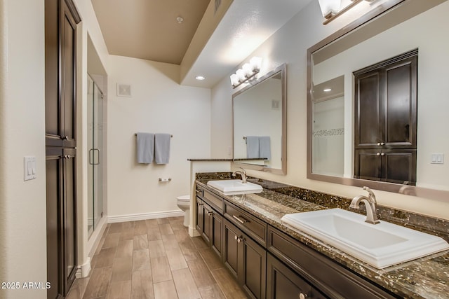 bathroom with baseboards, toilet, a shower stall, double vanity, and recessed lighting