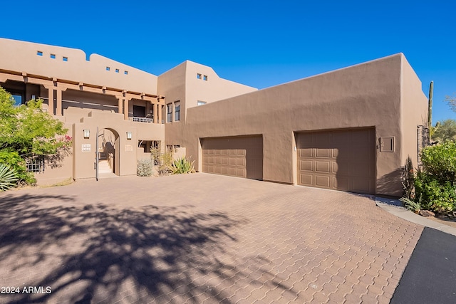 pueblo-style house featuring decorative driveway, a garage, and stucco siding