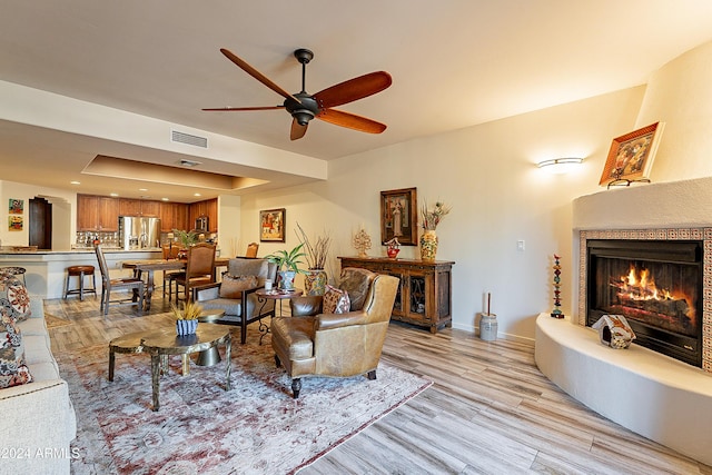 living room featuring visible vents, baseboards, a warm lit fireplace, and light wood finished floors