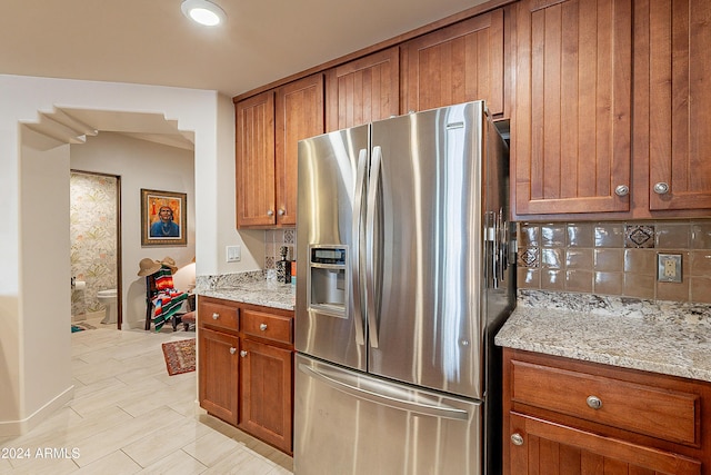 kitchen with brown cabinets, tasteful backsplash, stainless steel refrigerator with ice dispenser, and light stone countertops