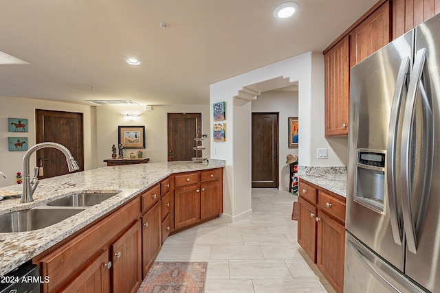 kitchen featuring a sink, light stone counters, stainless steel fridge, and brown cabinets