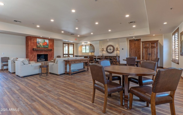 dining area with wood finished floors, recessed lighting, visible vents, and a large fireplace