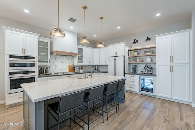 kitchen with white cabinetry, a center island with sink, and high end fridge