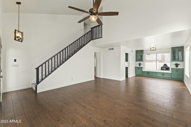 unfurnished living room with stairs, high vaulted ceiling, dark wood-style flooring, and ceiling fan with notable chandelier