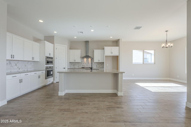 kitchen with white cabinetry, an island with sink, and wall chimney range hood