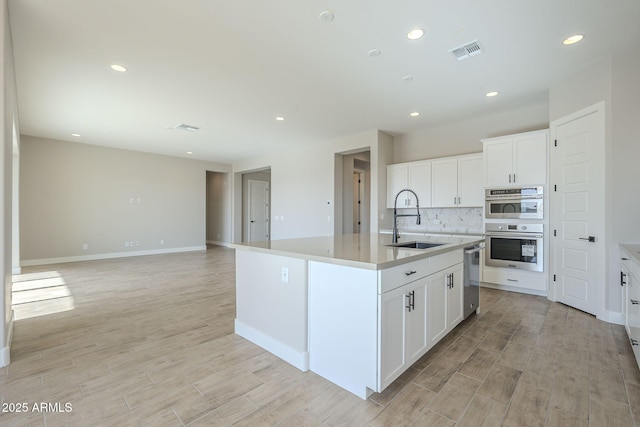 kitchen featuring decorative backsplash, stainless steel appliances, a kitchen island with sink, sink, and white cabinetry