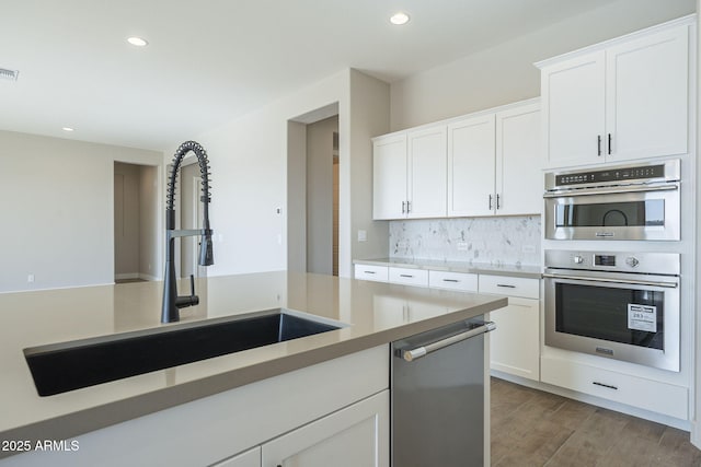 kitchen with sink, stainless steel appliances, decorative backsplash, white cabinets, and hardwood / wood-style flooring