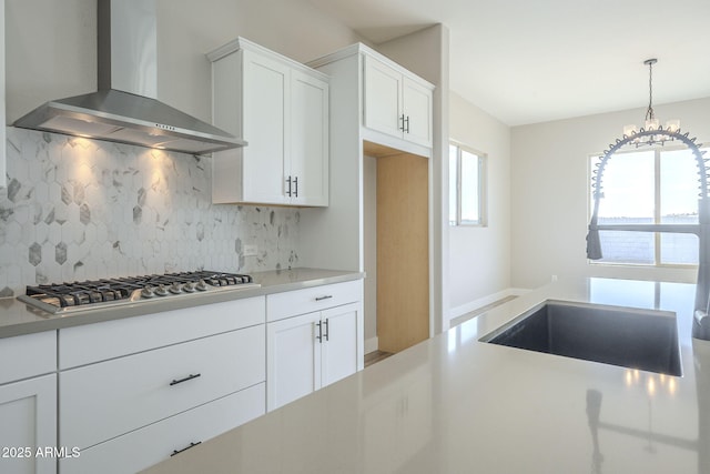 kitchen with decorative backsplash, sink, wall chimney range hood, white cabinets, and stainless steel gas stovetop