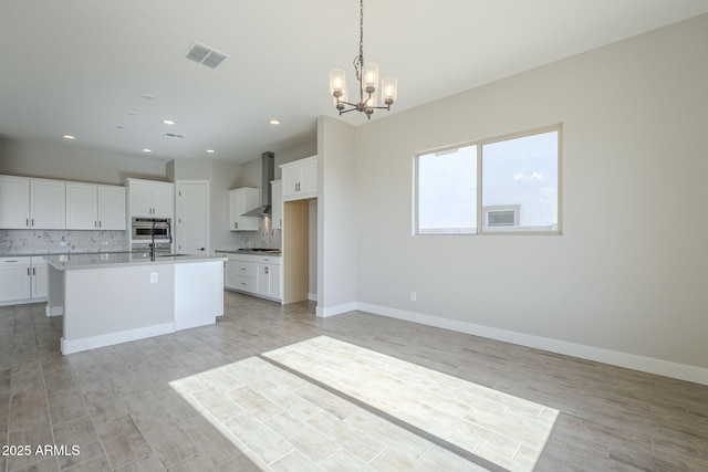 kitchen featuring pendant lighting, a kitchen island with sink, white cabinets, wall chimney range hood, and tasteful backsplash