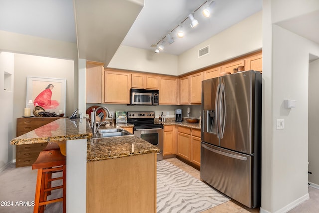 kitchen with sink, a kitchen bar, kitchen peninsula, stainless steel appliances, and dark stone countertops