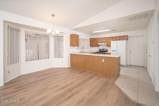 kitchen featuring white refrigerator with ice dispenser, stainless steel range with electric stovetop, brown cabinetry, under cabinet range hood, and visible vents