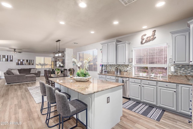 kitchen with a center island, stainless steel dishwasher, sink, decorative light fixtures, and gray cabinets