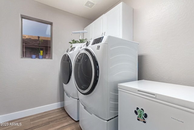 washroom with cabinets, wood-type flooring, and washing machine and clothes dryer